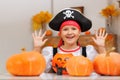 Celebrating Halloween at home. A cheerful little girl in a pirate costume sits at a table with pumpkins and a bucket