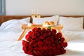 Celebrating Saint Valentine`s Day with bouquet of red roses, glass of champagne and croissants on tray on bed Royalty Free Stock Photo