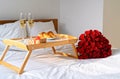 Celebrating Saint Valentine`s Day with bouquet of red roses, glass of champagne and croissants on tray on bed. Romantic surprise Royalty Free Stock Photo