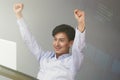 Celebrating success. Excited young Asian businessman arms up while working at office with laptop. Royalty Free Stock Photo