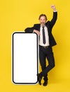 Celebrating victory with one hand raised in the air handsome businessman in black suit leaned on big smartphone with Royalty Free Stock Photo