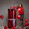 Celebrating young girl jumping under confetti with red gifts and balloons, holiday sale and discount concept