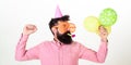 Celebration concept. Guy in party hat with air balloons celebrates. Man with beard and mustache on busy face blows into Royalty Free Stock Photo