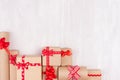 Celebration gifts background - different presents of craft paper wrapped with red ribbons and bows on white wood table. Royalty Free Stock Photo