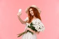 Celebration, social media and internet concept. Alluring sassy redhead female in straw hat, spring dress, holding