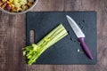 Celery stalks washed and ready to chop on a black cutting board, chef knife, wood table Royalty Free Stock Photo