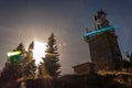 Cell phone relay tower on the mountain. Sunlight between some fir trees. Mountain cable transport on background