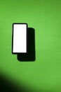 Cell phone with white screen on top of a green table. smartphone concept. Royalty Free Stock Photo