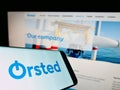 Cellphone with business logo of Danish energy company ÃËrsted AS on screen in front of webpage.