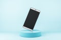 Cellphone frame with blank black screen standing on one corner on turquoise cylinder at abstract blue background. Realistic cell Royalty Free Stock Photo