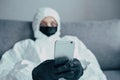 A cellphone in the hands of virologist in viral protective suit with a medical face mask and searching for information on the soci