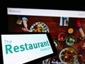 Cellphone with logo of British gastronomy company The Restaurant Group plc on screen in front of website.