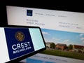 Cellphone with logo of British housebuilding company Crest Nicholson plc on screen in front of website.