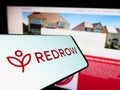 Cellphone with logo of British housebuilding company Redrow plc on screen in front of business website.