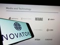 Cellphone with logo of British private equity firm Novator Partners LLP on screen in front of webpage.