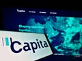 Cellphone with logo of British process outsourcing company Capita plc on screen in front of website with map.