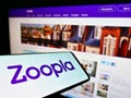 Cellphone with logo of British real estate platform Zoopla Limited on screen in front of business web page.