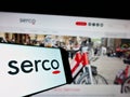Cellphone with logo of British service company Serco Group plc on screen in front of business website.
