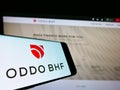 Cellphone with logo of Franco-German financial company Oddo BHF AG on screen in front of business webpage.