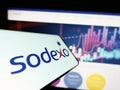 Cellphone with logo of French facility management company Sodexo S.A. on screen in front of website.