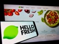 Cellphone with logo of German meal-kit company HelloFresh SE on screen in front of business website.