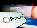 Cellphone with logo of payments company Payoneer Global Inc. on screen in front of business website.