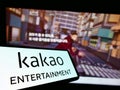 Cellphone with logo of South Korean company Kakao Entertainment Corp. on screen in front of business webpage.