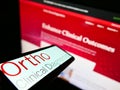 Cellphone with logo of US medical diagnostics company Ortho Clinical Diagnostics on screen in front of website.