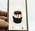 Cellphone recording cupcake with one candle burning with white background Royalty Free Stock Photo