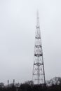A cellular communications tower, with many antennas, in dense fog, haze hazy into the sky, against a dull gray sky, trees and a Royalty Free Stock Photo