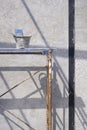 Cement bucket with plastering tools on scaffolding with sunlight and shadow on concrete wall surface in house construction site