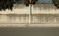 Cement pole on sidewalk with precast concrete wall on behind. Branches of tree on top, urban street in front Royalty Free Stock Photo