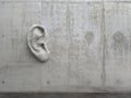 Cement sculpture in the shape of a human ear on a concrete wall. Illustration of the metaphor