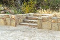 Cement stone stair case with four steps and small rock retaining wall with dirt floor and nature background