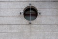 A cement wall with a porthole window with a gray painted cross grille Royalty Free Stock Photo