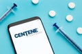 Centene corporation logo on Smart phone screen pills and syringe on blue background