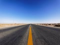 Centered view of an endless asphalt road in desert, low angle straight rough road with blue sky background, magic world Royalty Free Stock Photo