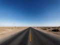 Centered view of an endless asphalt road in desert, low angle straight rough road with blue sky background, magic world Royalty Free Stock Photo