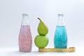 A centimeter, an apple, a pear and glass bottles with pink and blue basil seed stand on a white background