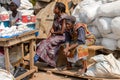 Unidentified Ghanaian women sit on wooden bench near white bags