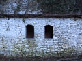 Century old house wall made of stone blocks, two window holes and green plants covering the roof. Brick works. Stone wall. Royalty Free Stock Photo