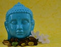 Ceramic Blue color Serene face statue of Buddha with flowers on colorful yellow background Royalty Free Stock Photo