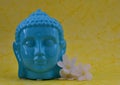 Ceramic Blue color Serene face statue of Buddha with flowers on colorful yellow background Royalty Free Stock Photo