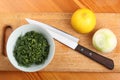 Ceramic bowl with chopped dill leaves, lemon, onion and kitchen knife on a cutting board Royalty Free Stock Photo