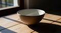 A ceramic bowl sits on a wooden table near a window. The light creates dramatic shadows and Royalty Free Stock Photo