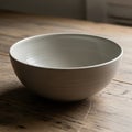 A ceramic bowl with a smooth light gray surface rests on a wooden table Royalty Free Stock Photo