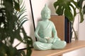 Ceramic Buddha sculpture with burning candle and books on wooden shelf indoors. Interior decor
