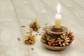 Ceramic candlestick and burning white wax candle, multicolored pine cones and coffee grains on light wooden background