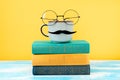 Ceramic cup of coffee with a felt moustache and glasses on the background of a stack of books. Concept of Father's
