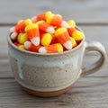 A ceramic cup filled with candy corn pieces sits on a wooden surface Royalty Free Stock Photo